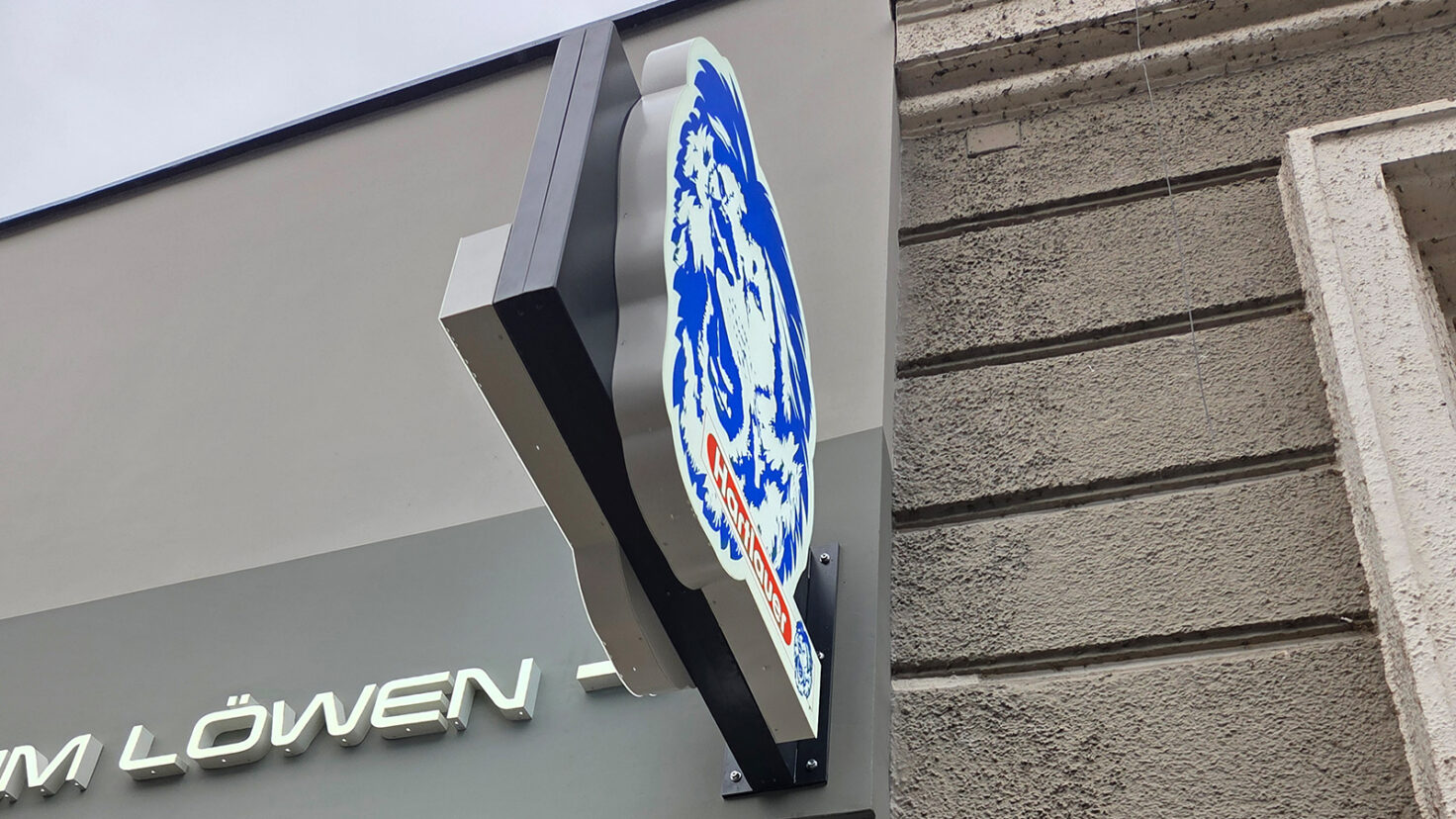 leuchtendes Steckschild an der Fassade der Hartlauer Filiale in Grieskirchen